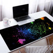 Custom Large Gaming Mouse Pad with vibrant paint splatter design on a desk with a laptop.