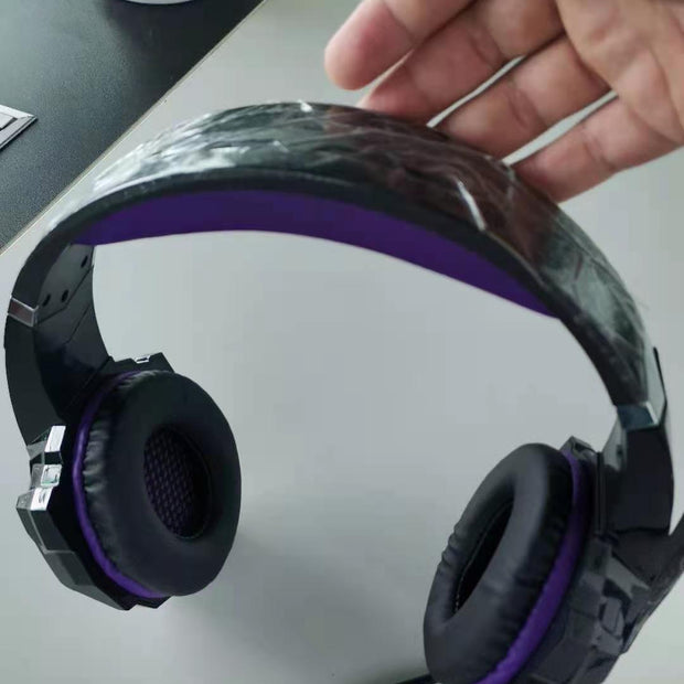 Black and purple headphones on a white surface with a hand holding the headband.
