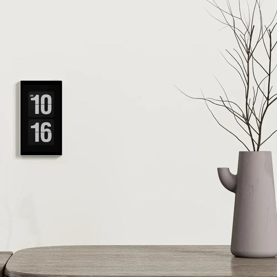 A stylish wall clock displaying the time 10:16 next to a modern vase on a wooden table.