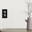 A stylish wall clock displaying the time 10:16 next to a modern vase on a wooden table.